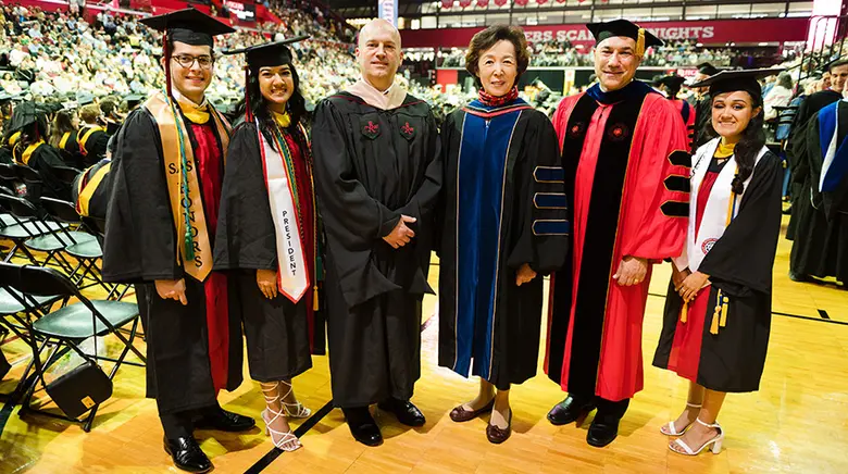 Rutgers Business School dean stands with convocation speaker and students.