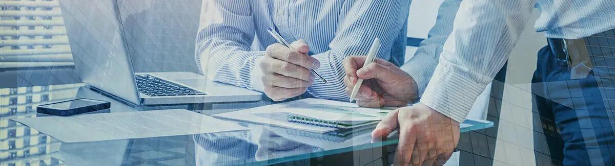 Closeup of two men holding pens over papers with analytical data