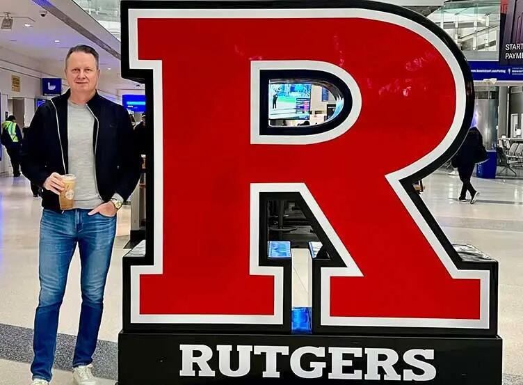 Dr. Andrew Evens, an alumnus of the Rutgers Executive MBA, stands at a Rutgers R sign at Newark International Airport.
