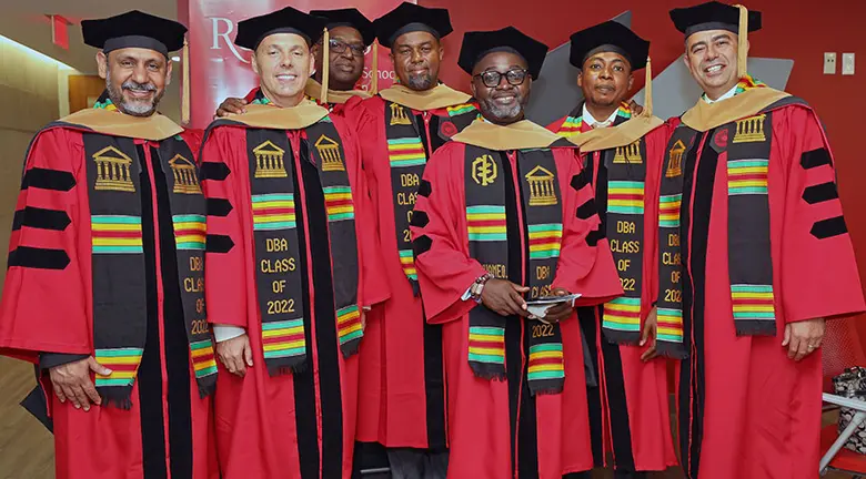 Seven students in traditional robes and hoods pose for a group shot following the presentation of their Doctoral of Business Administration degrees.