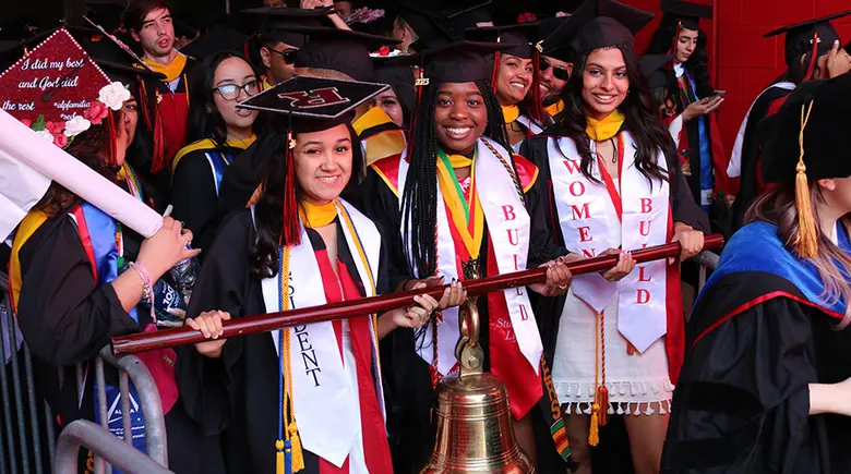 Three undergraduate Rutgers Business School students carry the school bell at the Rutgers University Commencement.