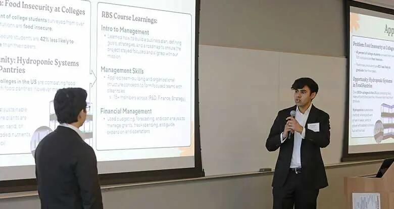 Léo Moreno listens as his classmate Rithik Kayadia presents information about Agrophonic Farms at Rutgers Business School's Experiential Learning Showcase..