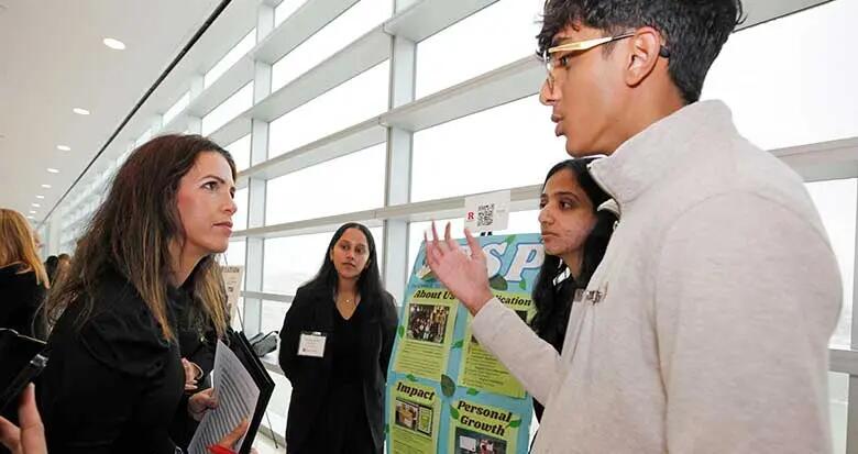 Rutgers MBA alumna Daniela Koumides, who helped to judge the competition, listens as members of a team explain their poster during the competition's first round.