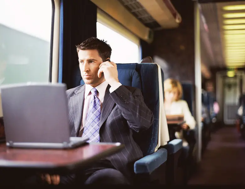 Man on a train on his cellphone with laptop in front of him