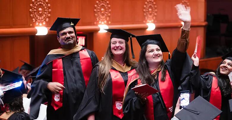 A group of jubilant graduates waves to friends and family in the crowd.