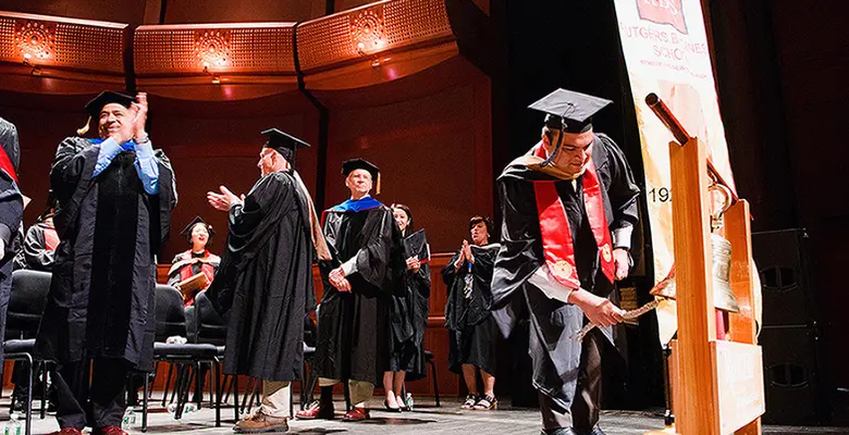 Mohit Hardikar rings the school bell marking the start of the graduate program commencement ceremony.