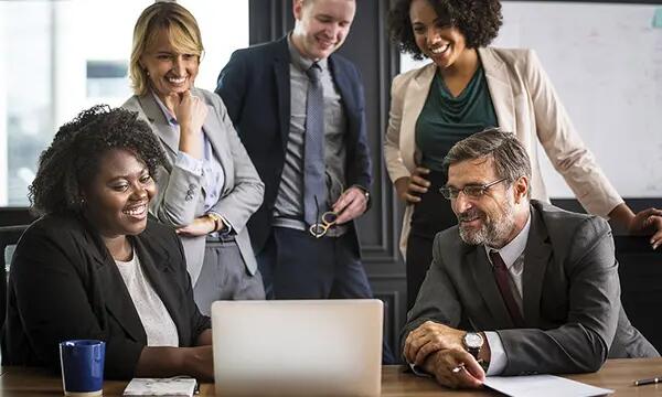 Group of people smiling while gathered in front of a laptop