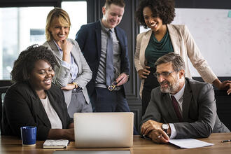 Group of people smiling while gathered in front of a laptop