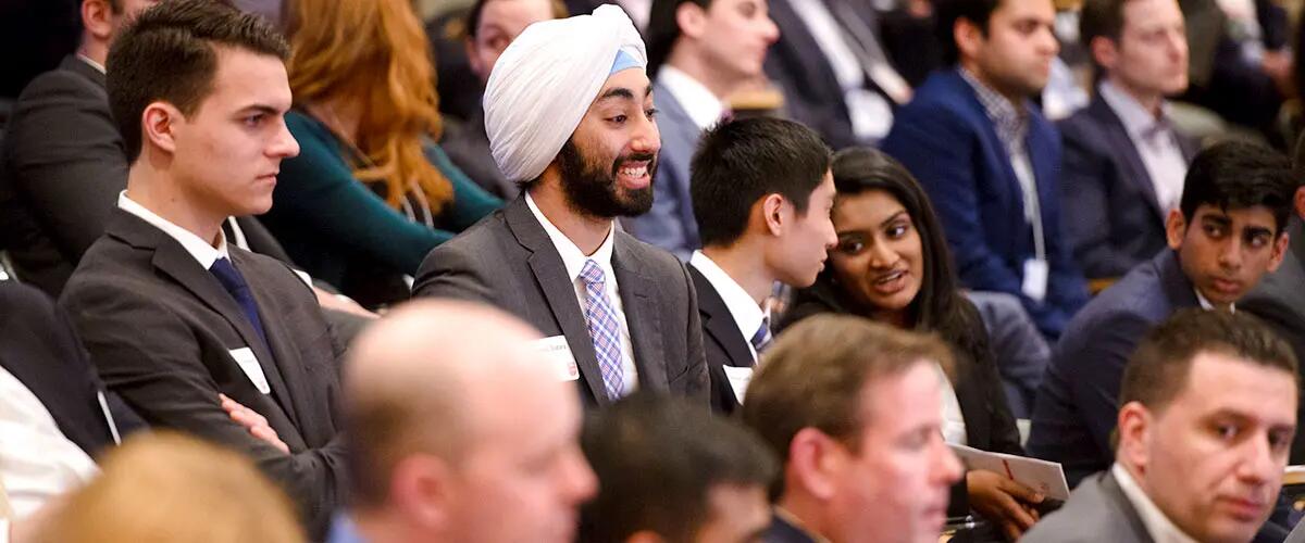 An assembly of people with varied expressions. A man in the center has a smile on his face.