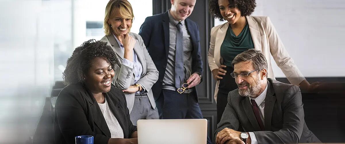 Group of people smiling while gathered in front of a laptop