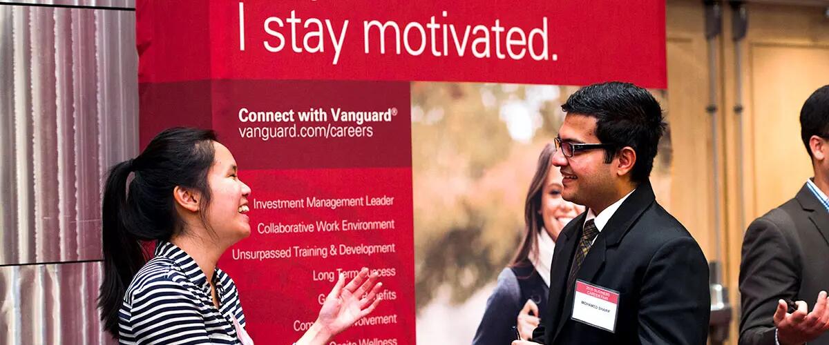 Students smiling at a career fair in front of the Vanguard Careers booth.
