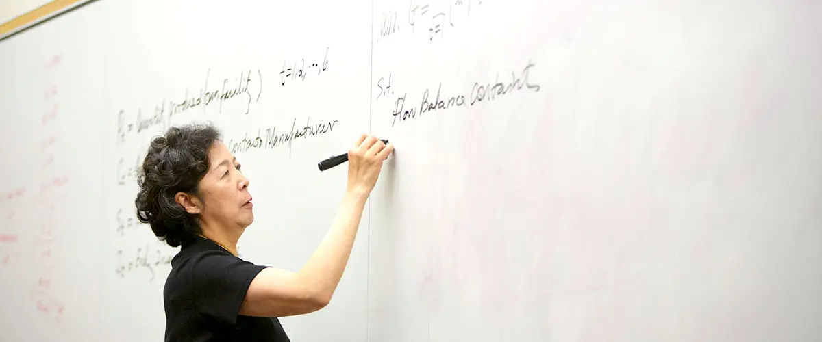 Dean Lei writes on a whiteboard during class.