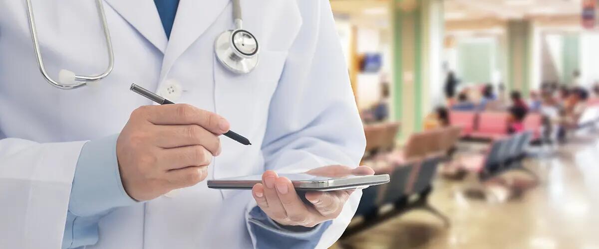 A doctor holds a tablet and stylus while wearing a stethoscope around their neck in a waiting room. 